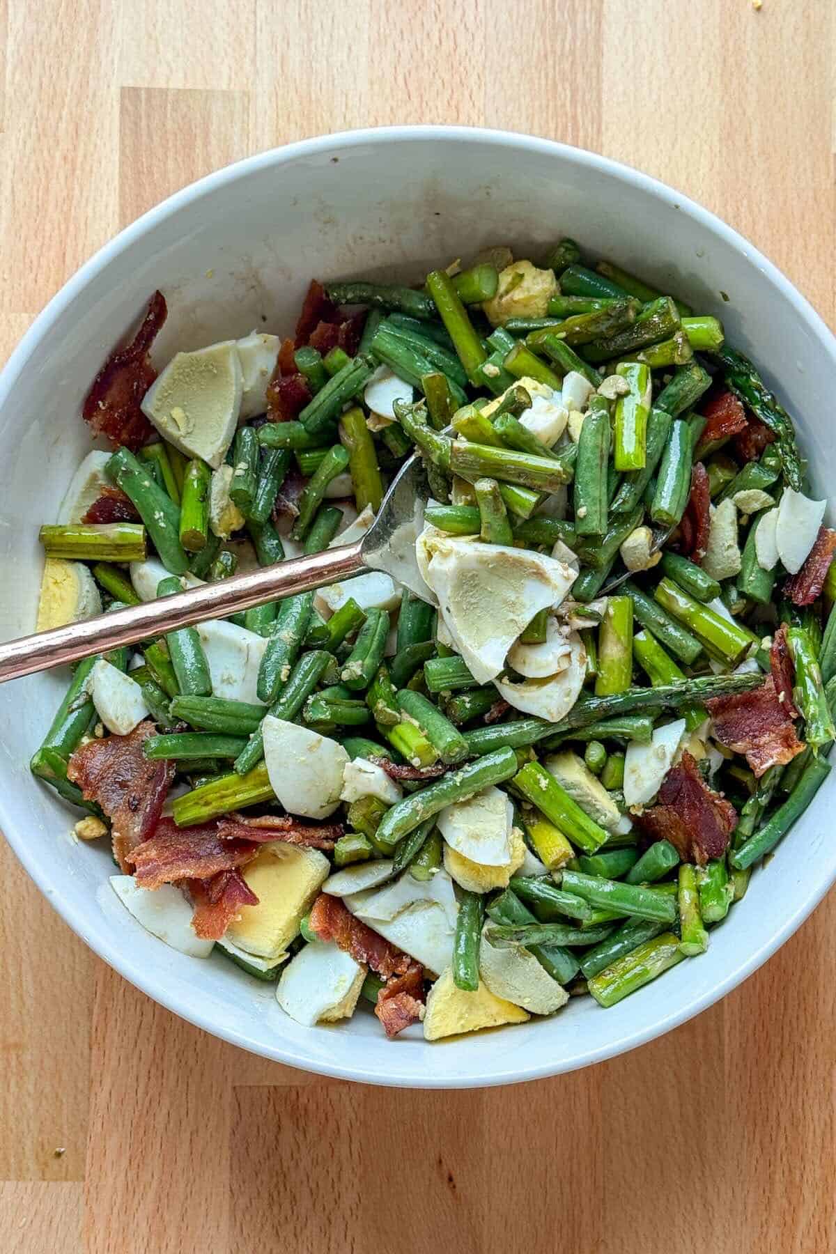 Roasted asparagus and green beans tossed with balsamic vinaigrette, hard boiled eggs and chopped bacon in a bowl.