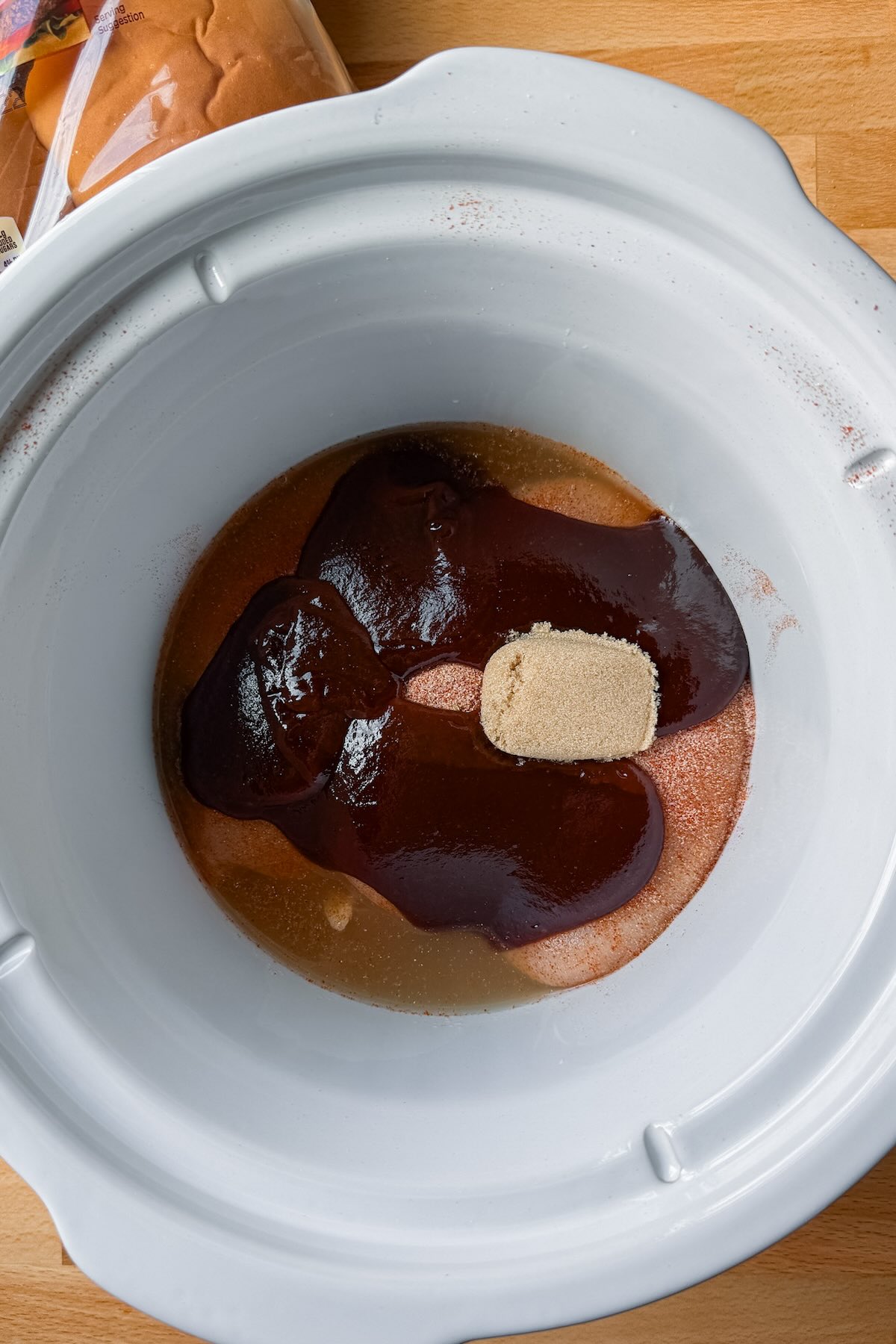 Seasoned chicken breasts with bbq sauce and slices in a round slow cooker.