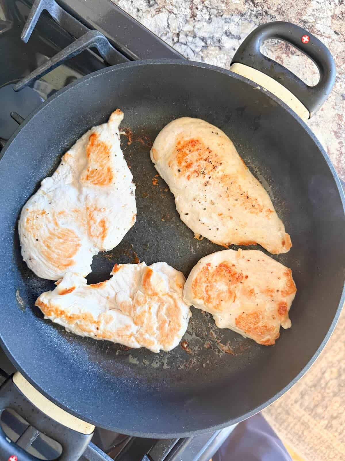 A skillet with browned chicken breasts.