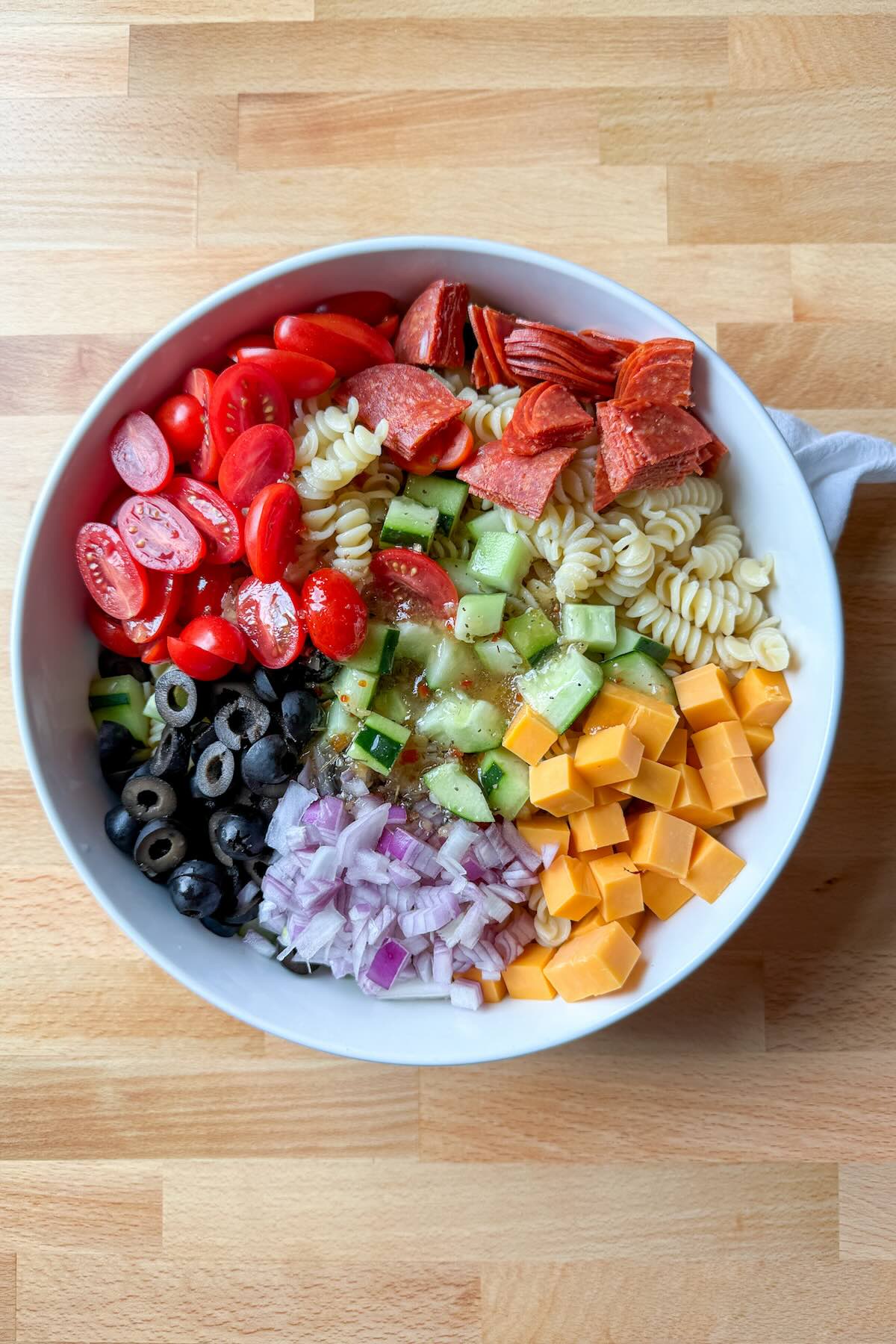 Chopped vegetables including tomatoes, cucumber, and red onion for pasta salad.