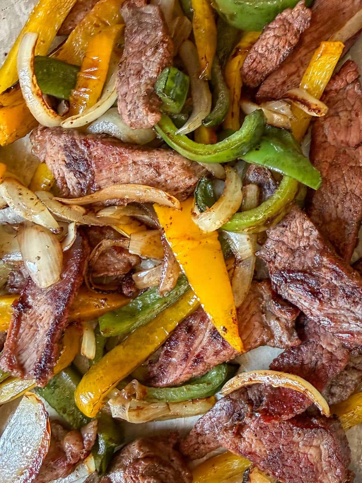 A close up of cooked beef fajitas on a sheet pan with peppers and onions.