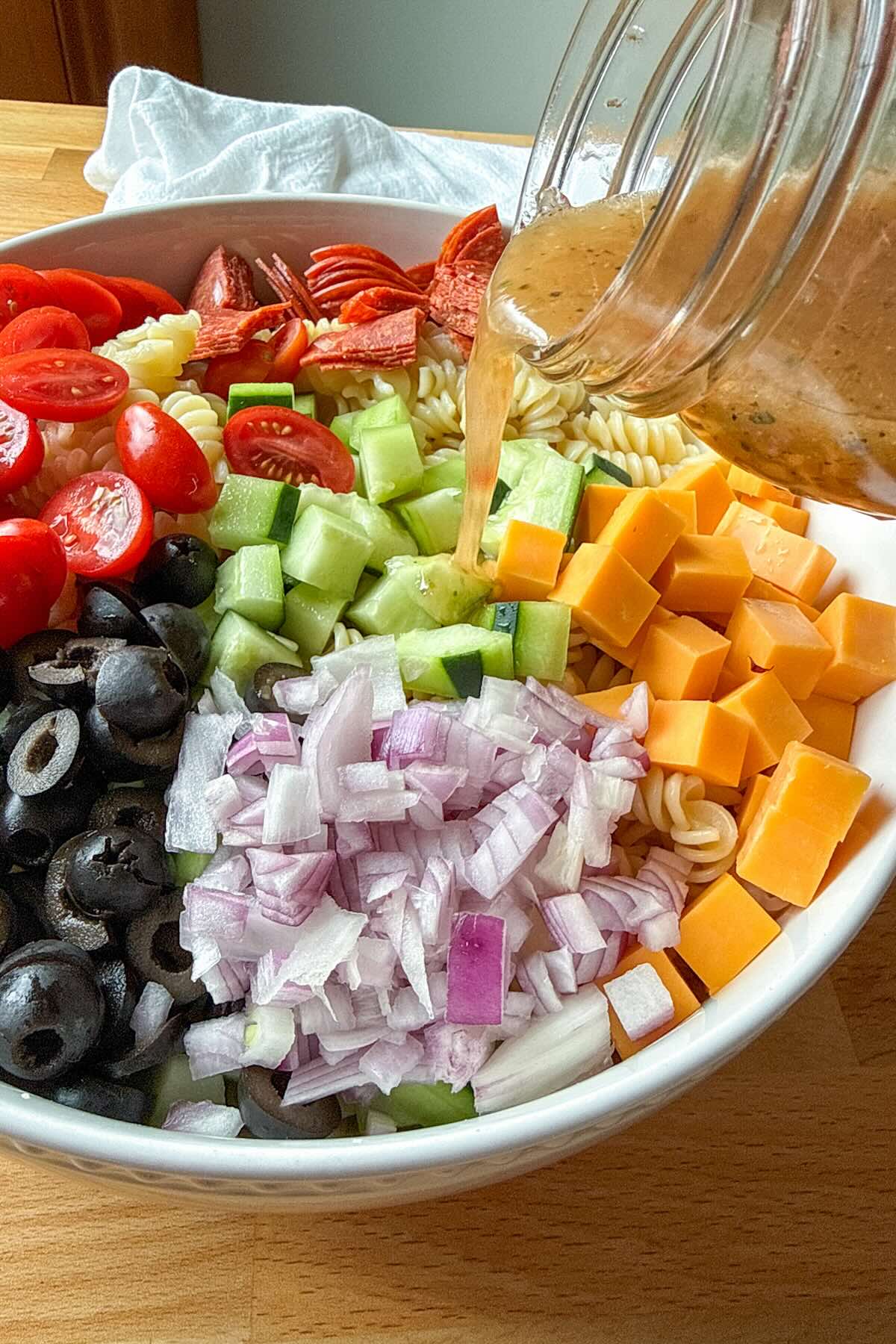 Pouring a shortcut Italian dressing over an easy Italian pasta salad pasta salad.