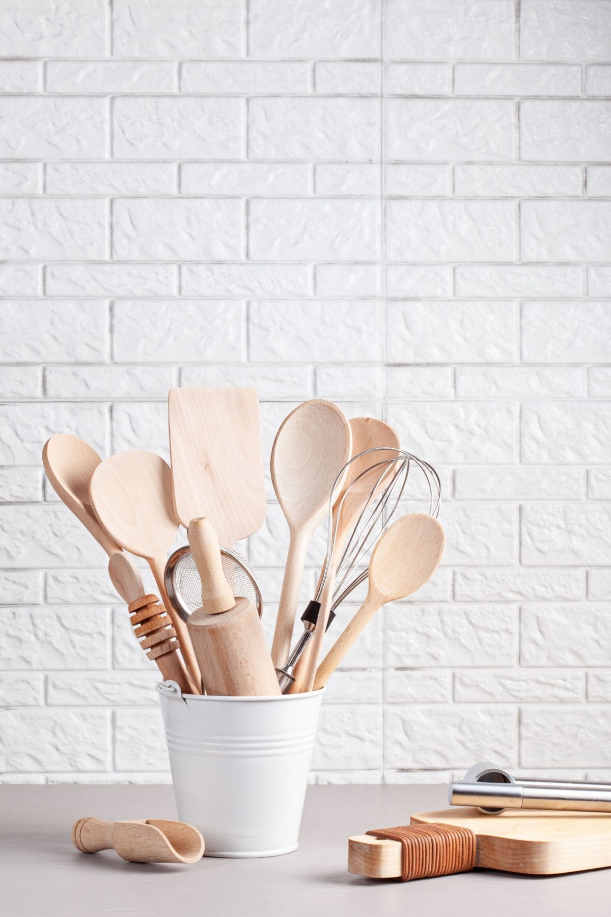 Kitchen utensils in a white container, including wooden spoons, spatulas, and a whisk, ideal for coo.