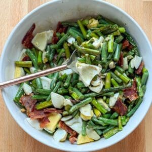 Roasted asparagus and green beans topped with bacon and hard boiled eggs in a serving bowl.
