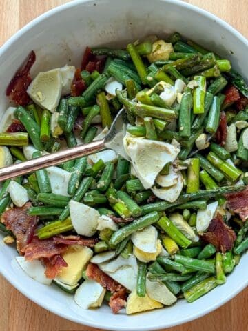 Roasted asparagus and green beans topped with bacon and hard boiled eggs in a serving bowl.