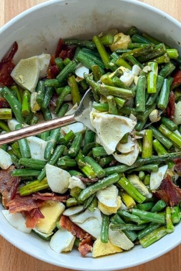 Roasted asparagus and green beans topped with bacon and hard boiled eggs in a serving bowl.