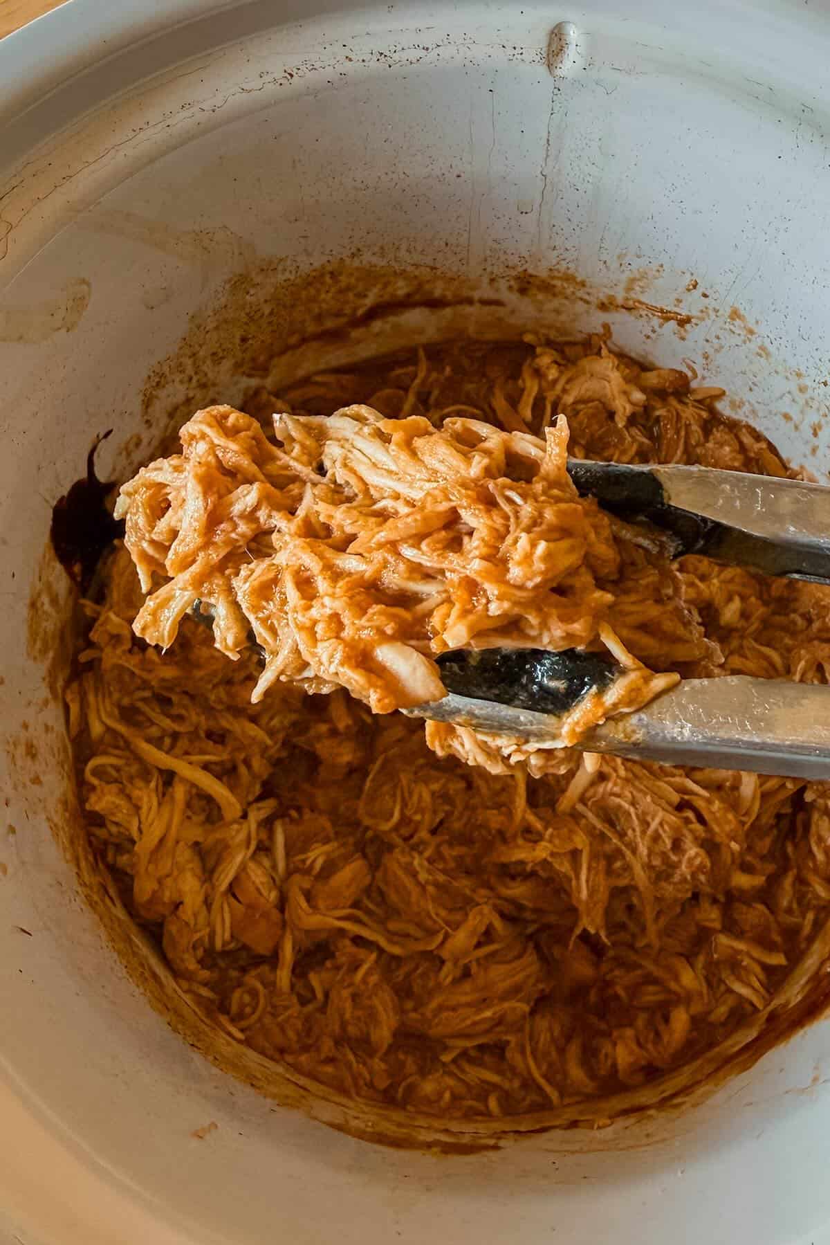 A close up of bbq shredded chicken held by tongs.