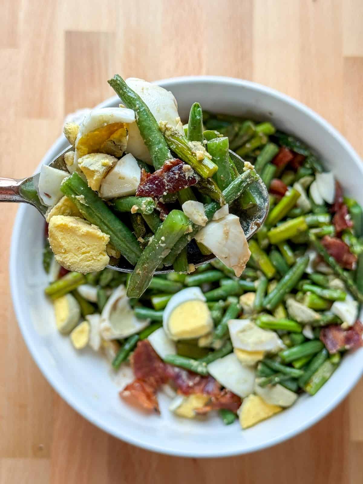 Spoonful of roasted asparagus and green beans with bacon and eggs ready to eat.