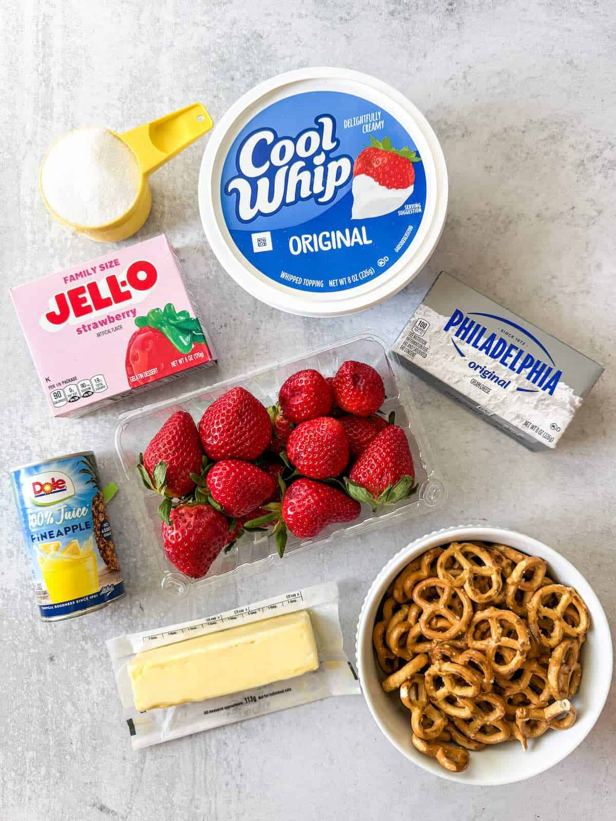 Ingredients to make strawberry pretzel salad with fresh strawberries, cool whip and pineapple juice.
