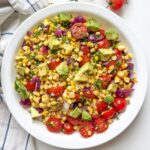 Grilled corn salad with avocado, cherry tomatoes, and lime juice served in a white bowl.