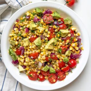 Grilled corn salad with avocado, cherry tomatoes, and lime juice served in a white bowl.