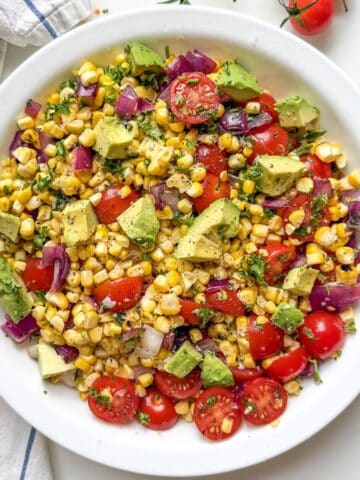 Grilled corn salad with avocado, cherry tomatoes, and lime juice served in a white bowl.