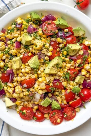 Grilled corn salad with avocado, cherry tomatoes, and lime juice served in a white bowl.