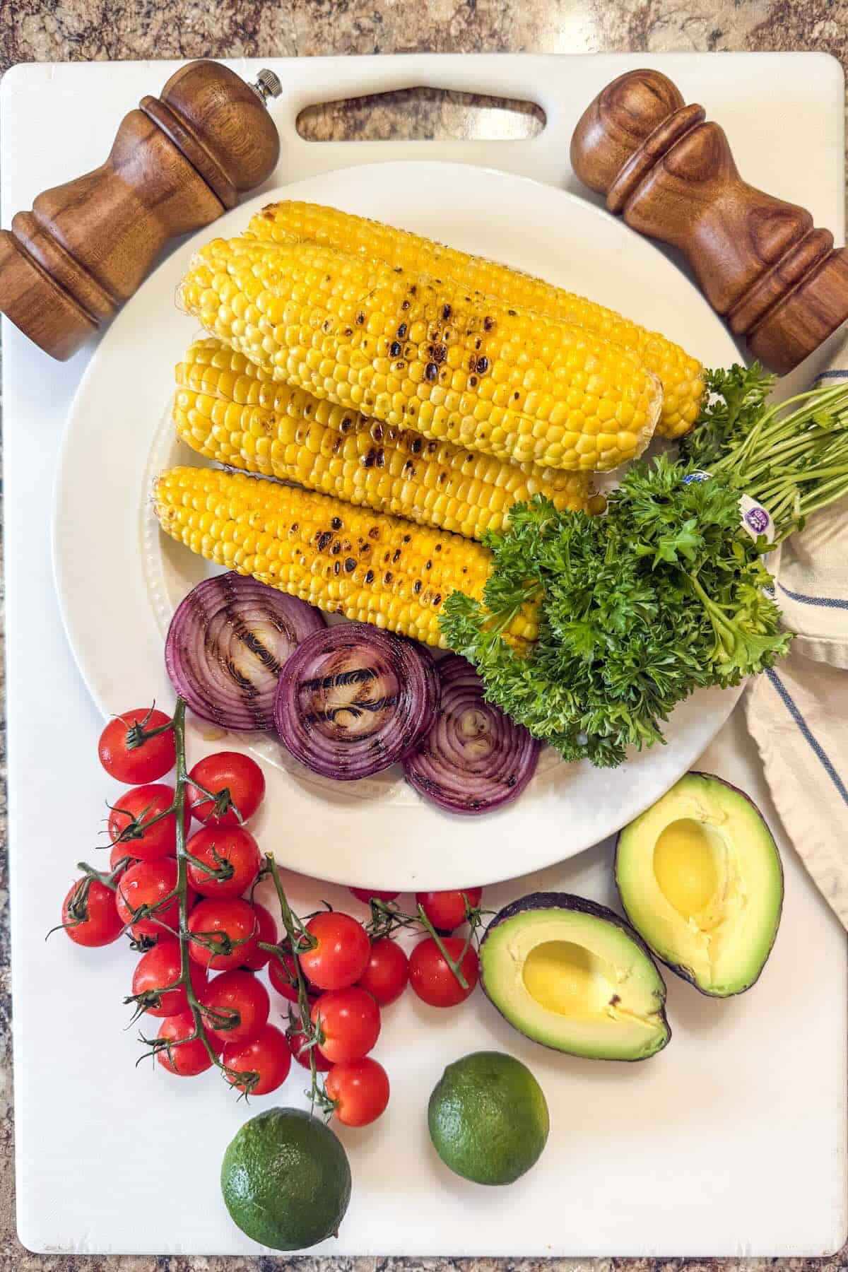 Grilled corn and onions on a platter alongside ingredients to make a corn salad.