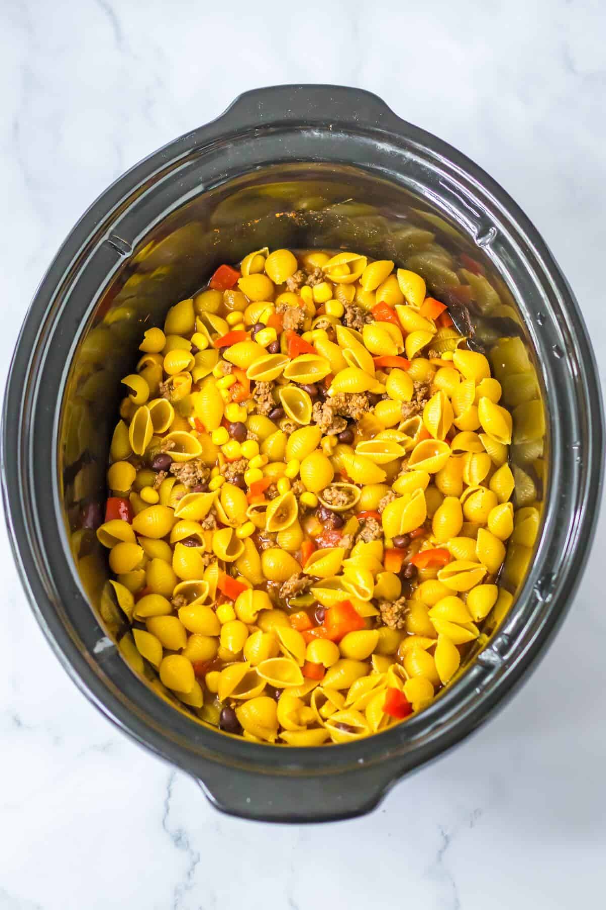 Short pasta being stirred into cheesy taco pasta in the slow cooker.