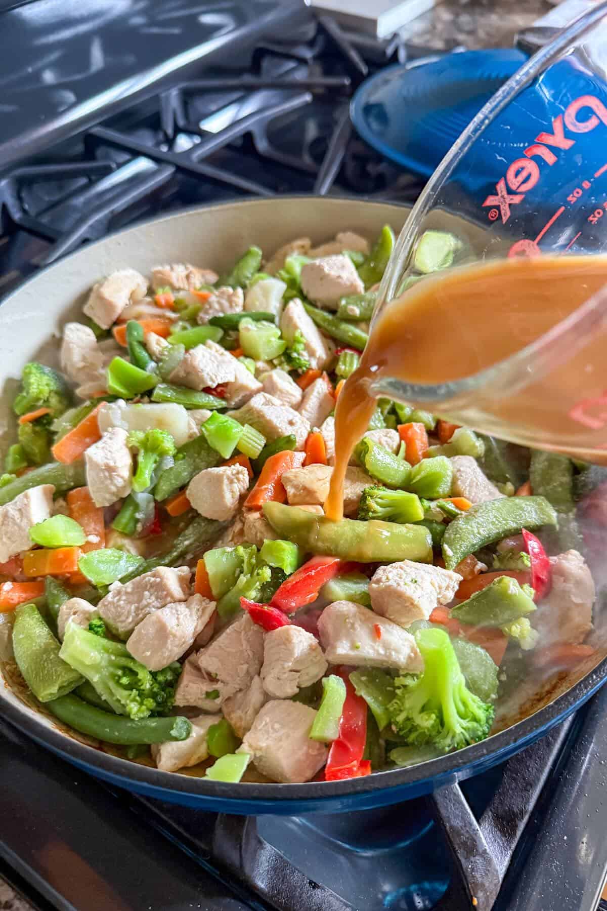 Adding a homemade stir fry sauce to the cooked vegetables and chicken.