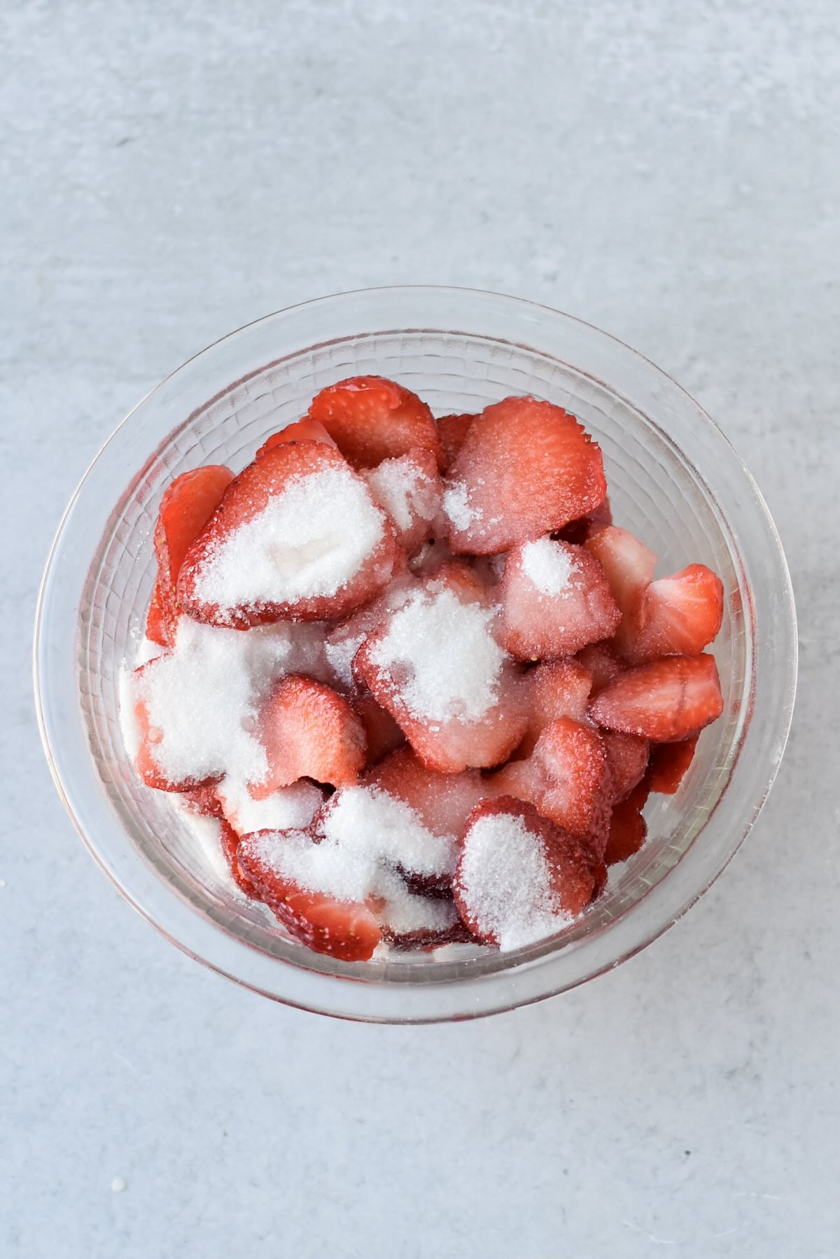 Adding sugar to sliced strawberries for macerated strawberry sauce.