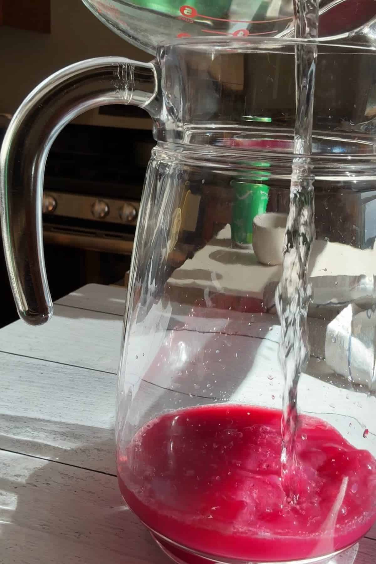 Pouring water into blueberry simple syrup and lemon juice.
