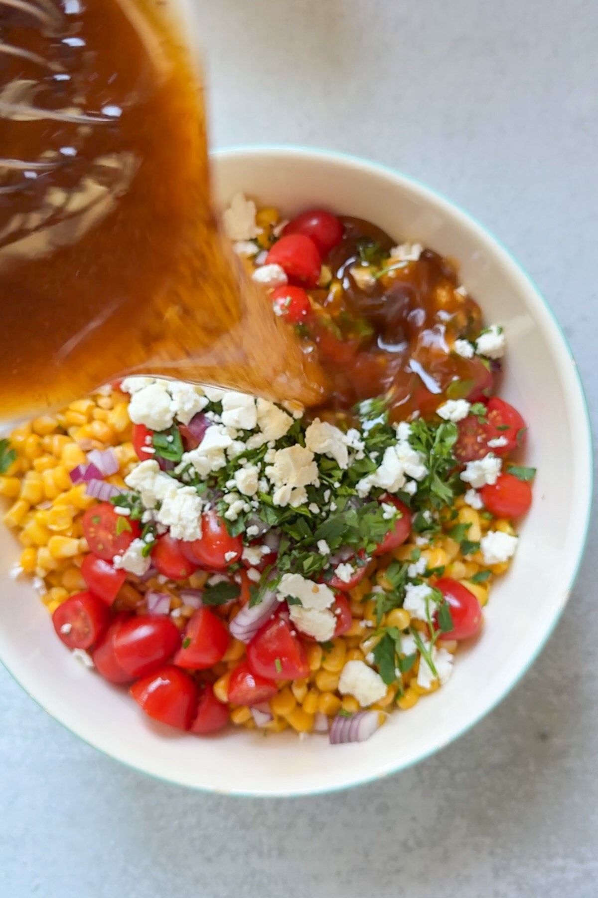 Pouring a homemade dressing over the corn salad before tossing.