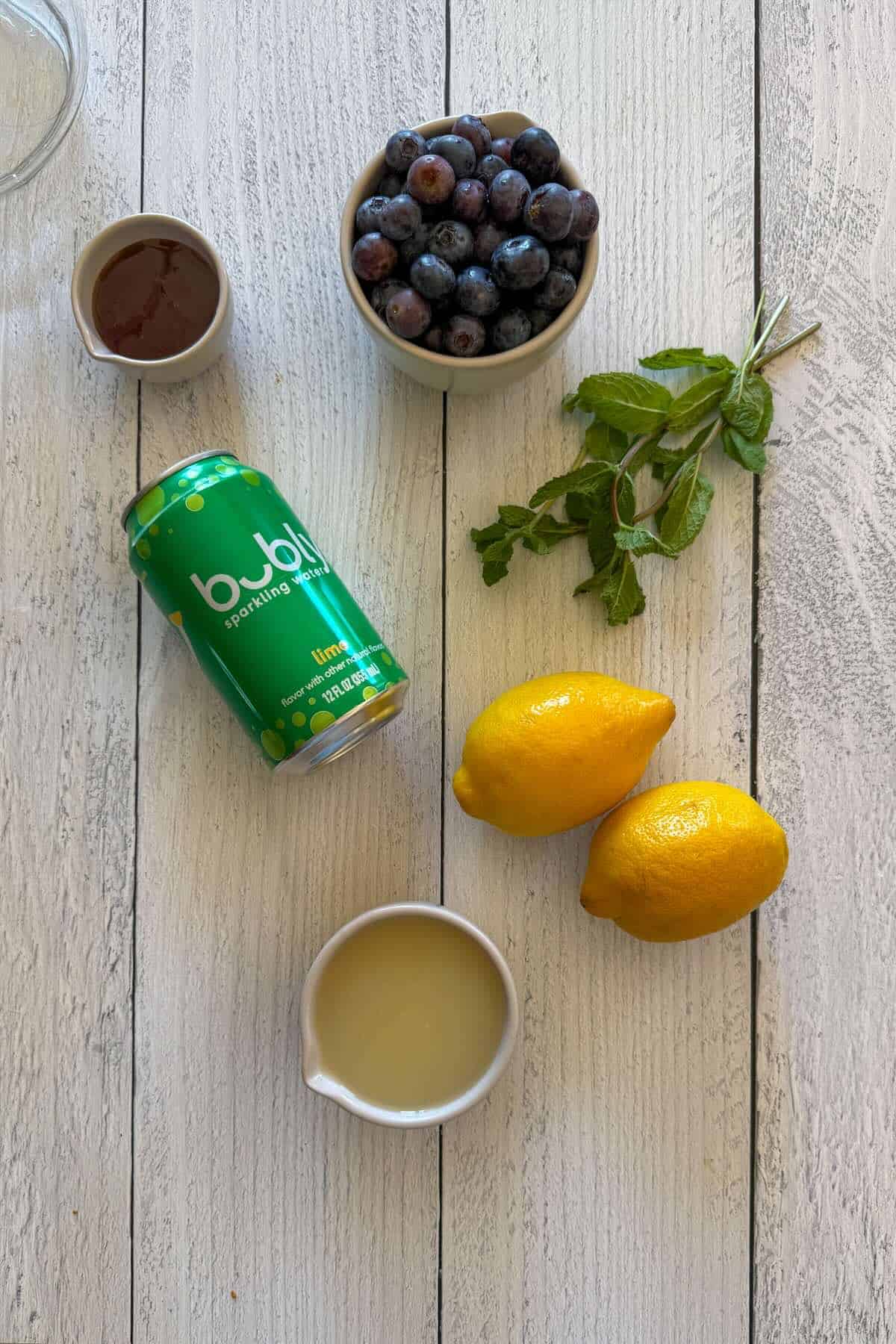 Ingredients to make a blueberry lemonade with mint, honey, and bubbly water.