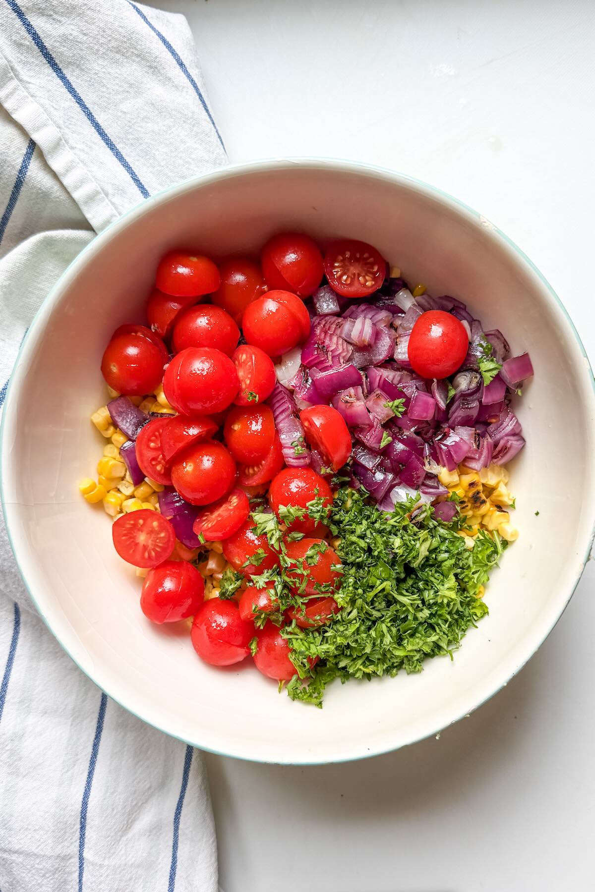 Charred corn, sliced cherry tomatoes, grilled onions and fresh parsley in a bowl.