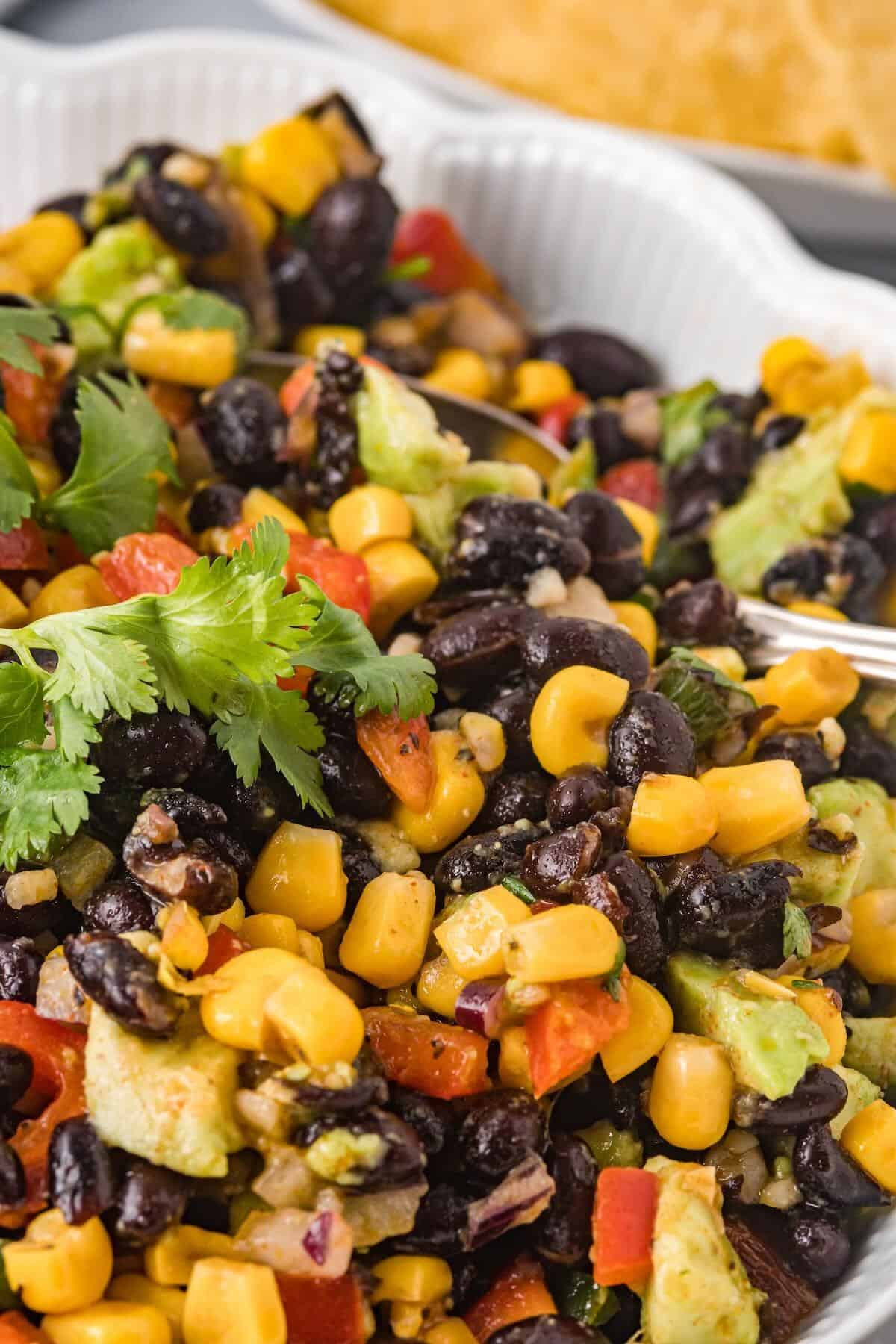Tortilla chip scooping cowboy caviar with beans, corn, peppers, and avocado.