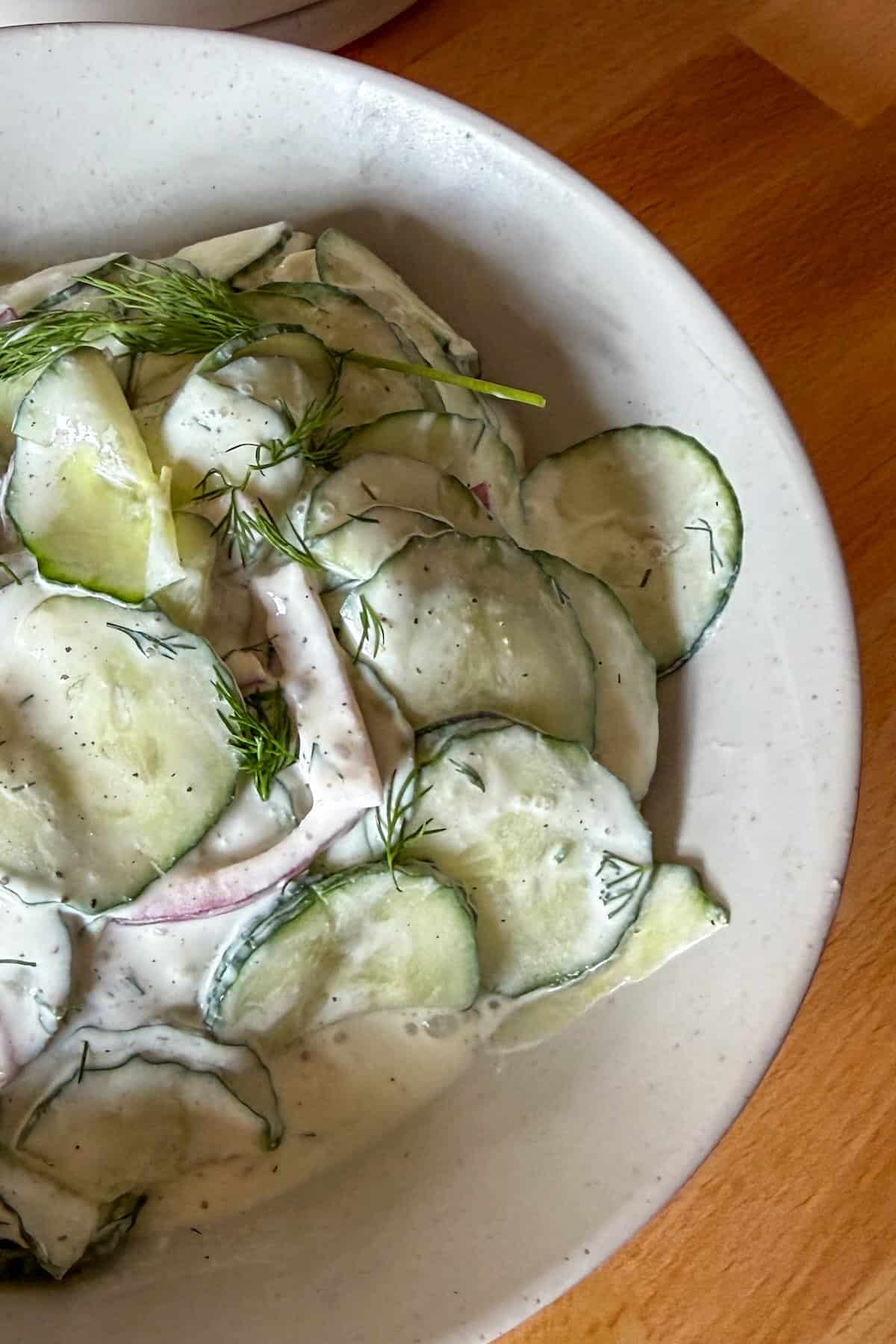 Close up of creamy cucumber dill salad with sliced onions and sour cream dressing.