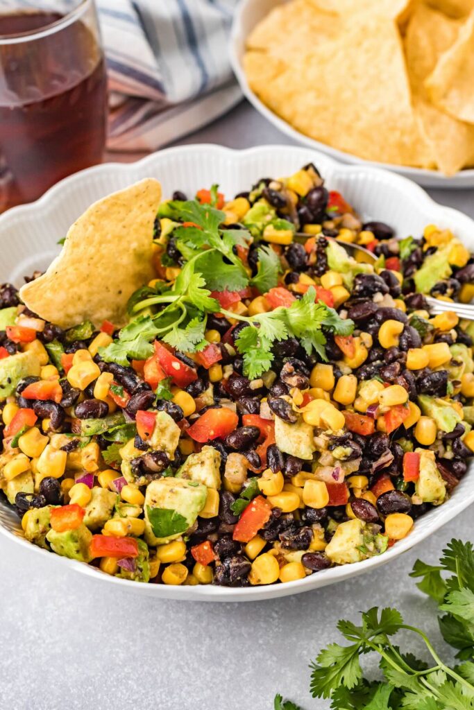 Cowboy caviar dip with black beans, corn, avocado, and tortilla chips in a serving bowl.