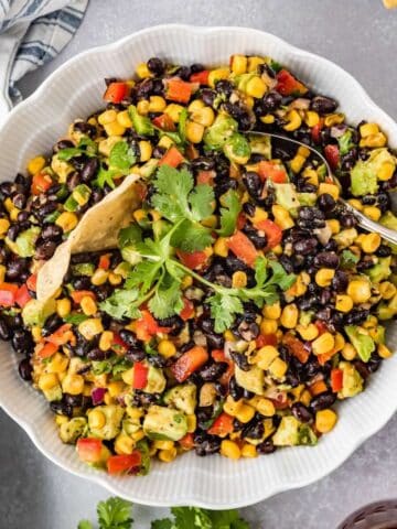Cowboy caviar dip with black beans, corn, avocado, and tortilla chips in a serving bowl.