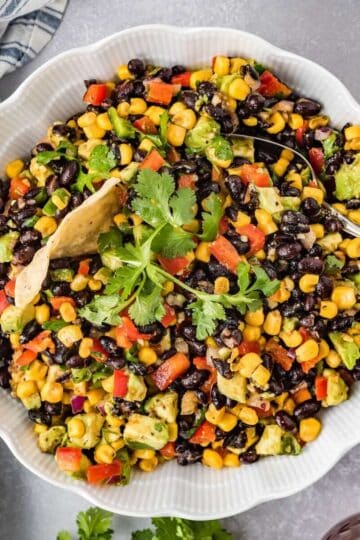 Cowboy caviar dip with black beans, corn, avocado, and tortilla chips in a serving bowl.
