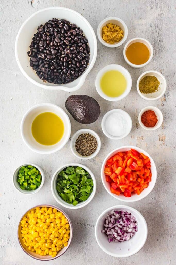 Ingredients for cowboy caviar including black beans, corn, peppers, avocado, cilantro, and lime juice.