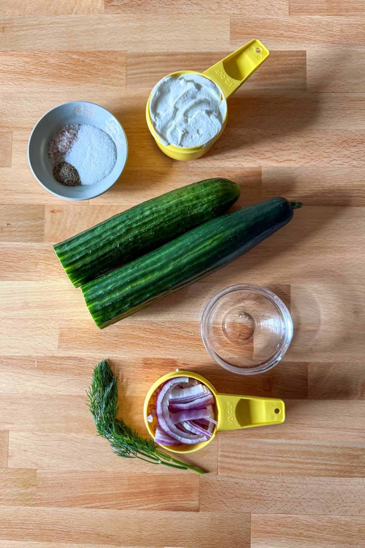 Ingredients for creamy cucumber salad including cucumbers sour cream dill and onion.