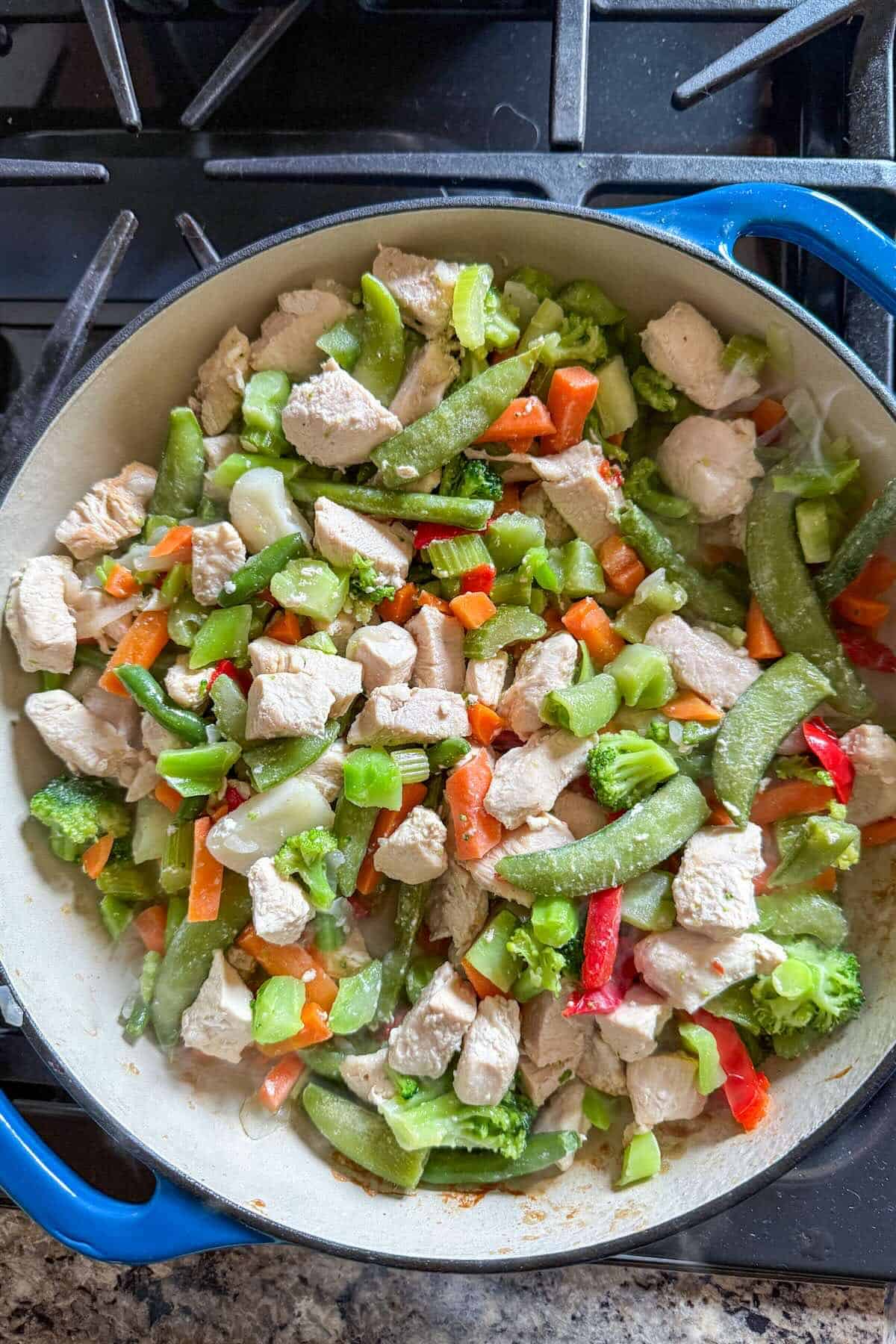 Frozen stir fry vegetables added to cooked chicken in a skillet.