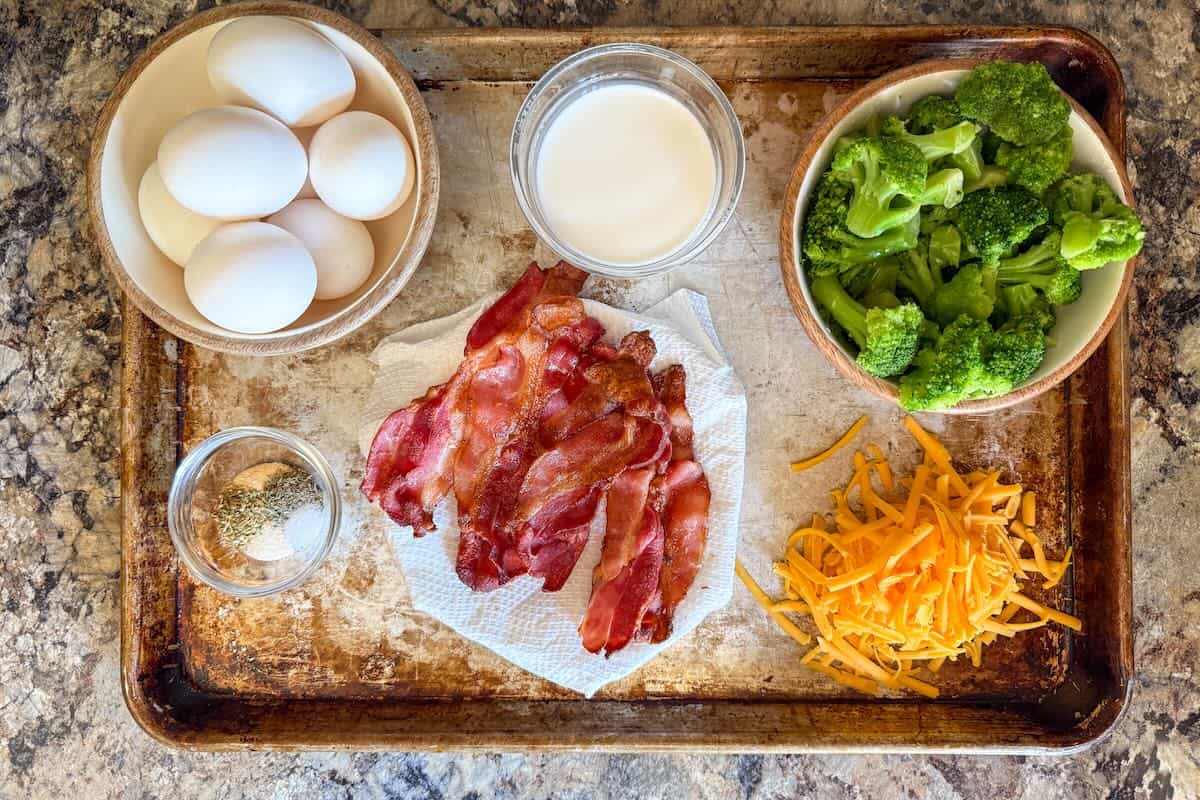 Ingredients for low carb bacon broccoli breakfast casserole including eggs, bacon, broccoli, cheddar cheese, and seasonings.