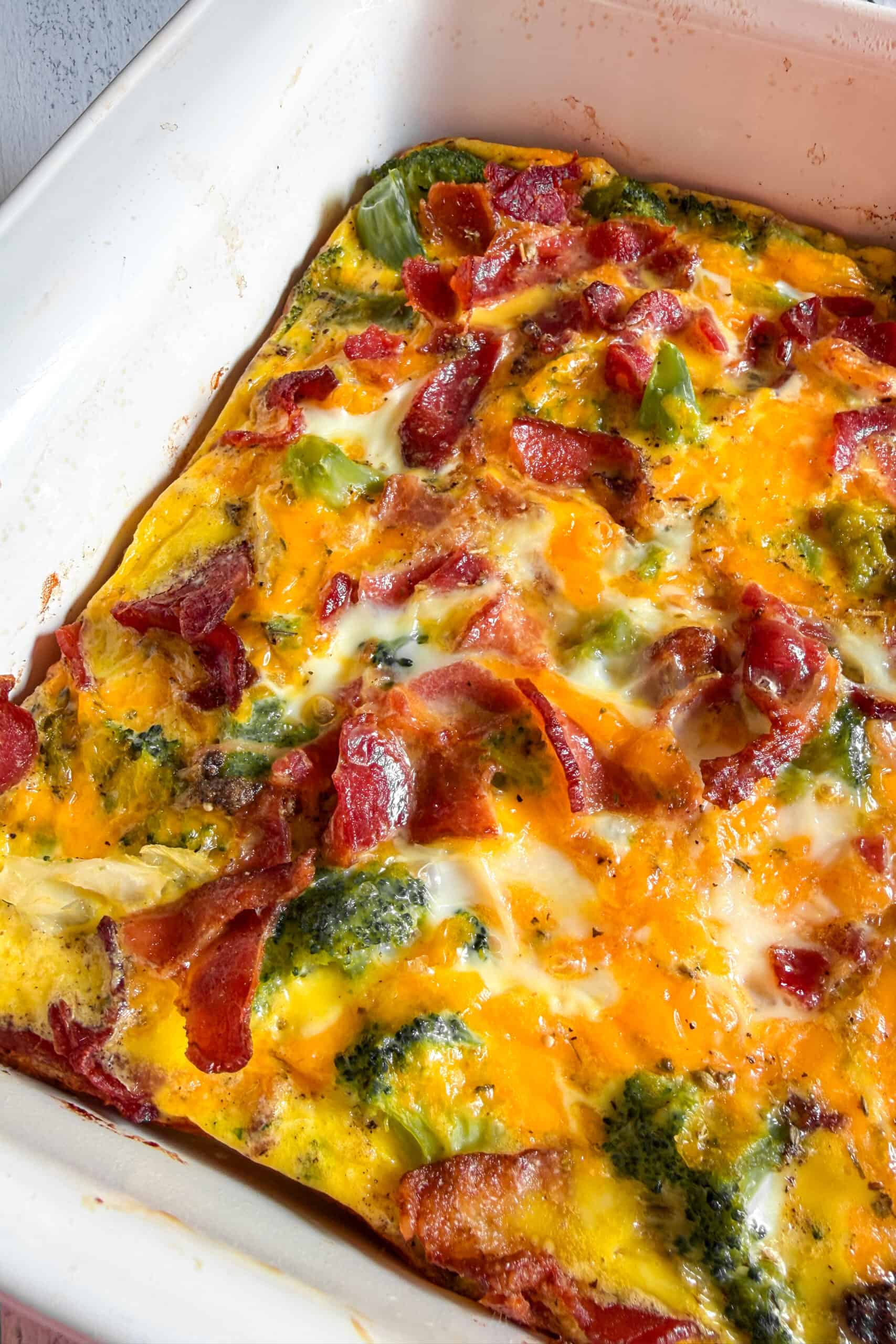 Low carb bacon broccoli breakfast casserole sliced in a baking dish with cheddar cheese and crispy bacon on top.