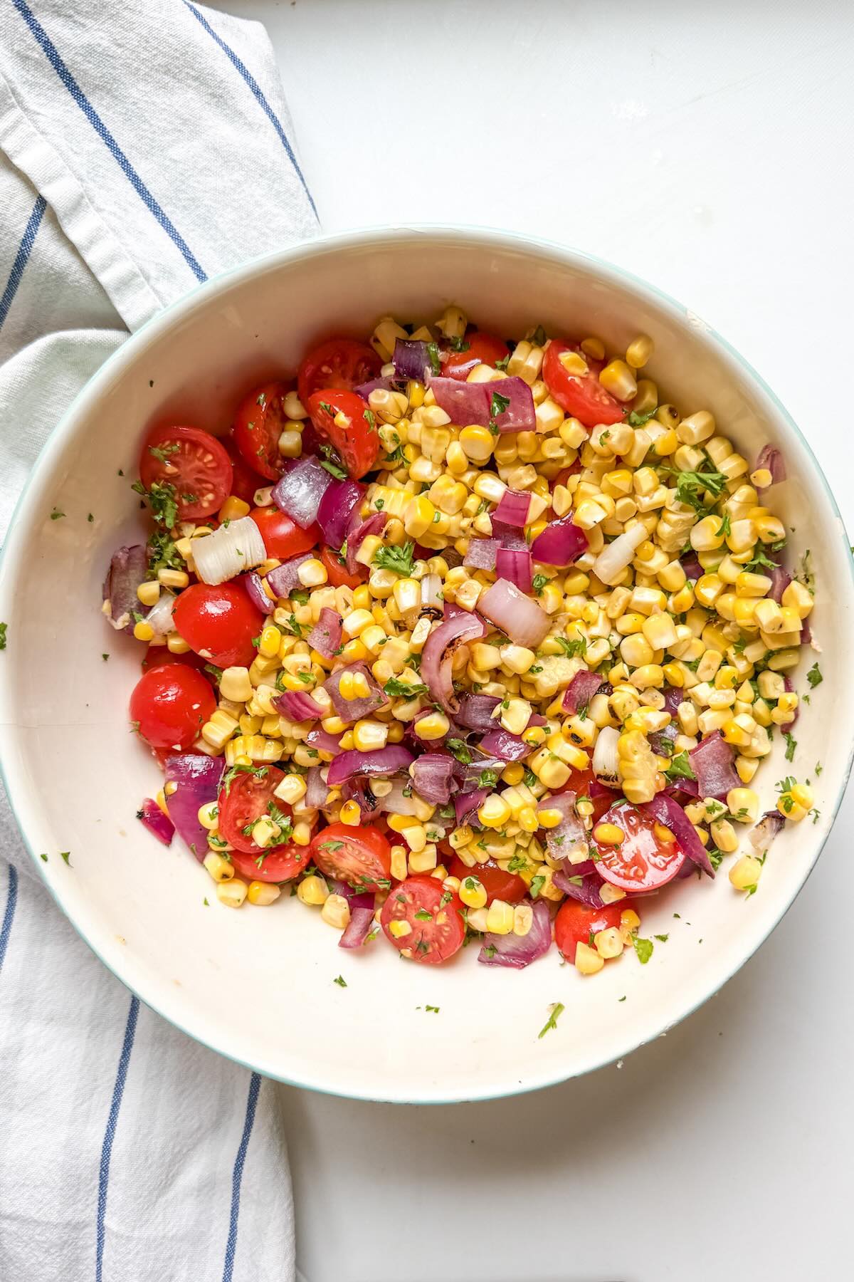 Tossed grilled corn salad with, tomatoes, and lime dressing in a large bowl.