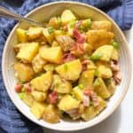 Rustic bowl of potato salad without mayo garnished with crispy bacon and sliced green onions.