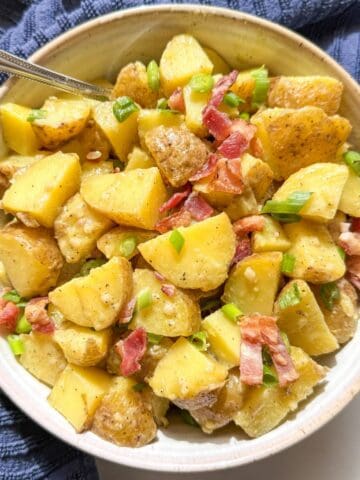 Rustic bowl of potato salad without mayo garnished with crispy bacon and sliced green onions.