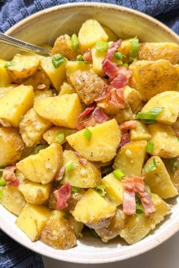 Rustic bowl of potato salad without mayo garnished with crispy bacon and sliced green onions.