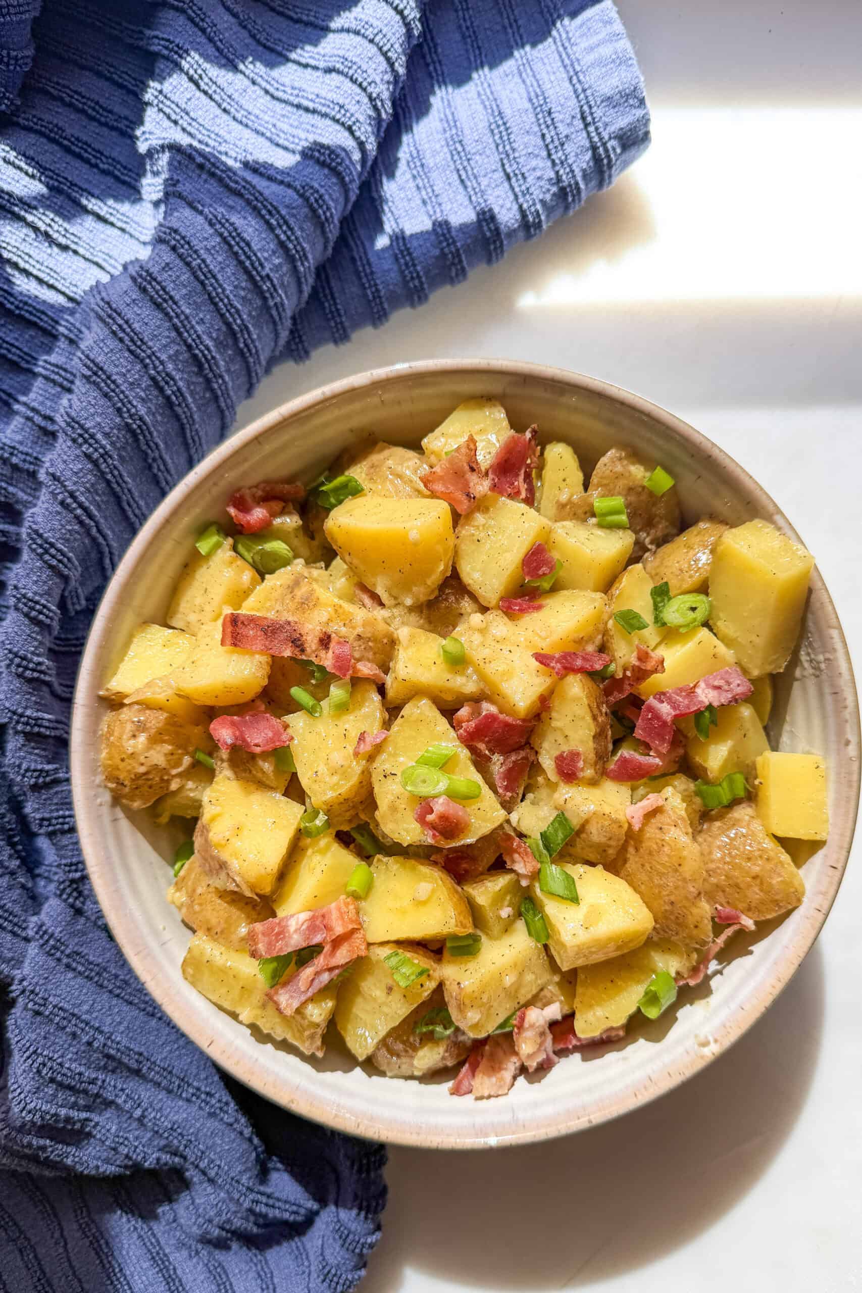 Homemade potato salad without mayonnaise served in a grey bowl with bacon crumbles and sliced green onions.