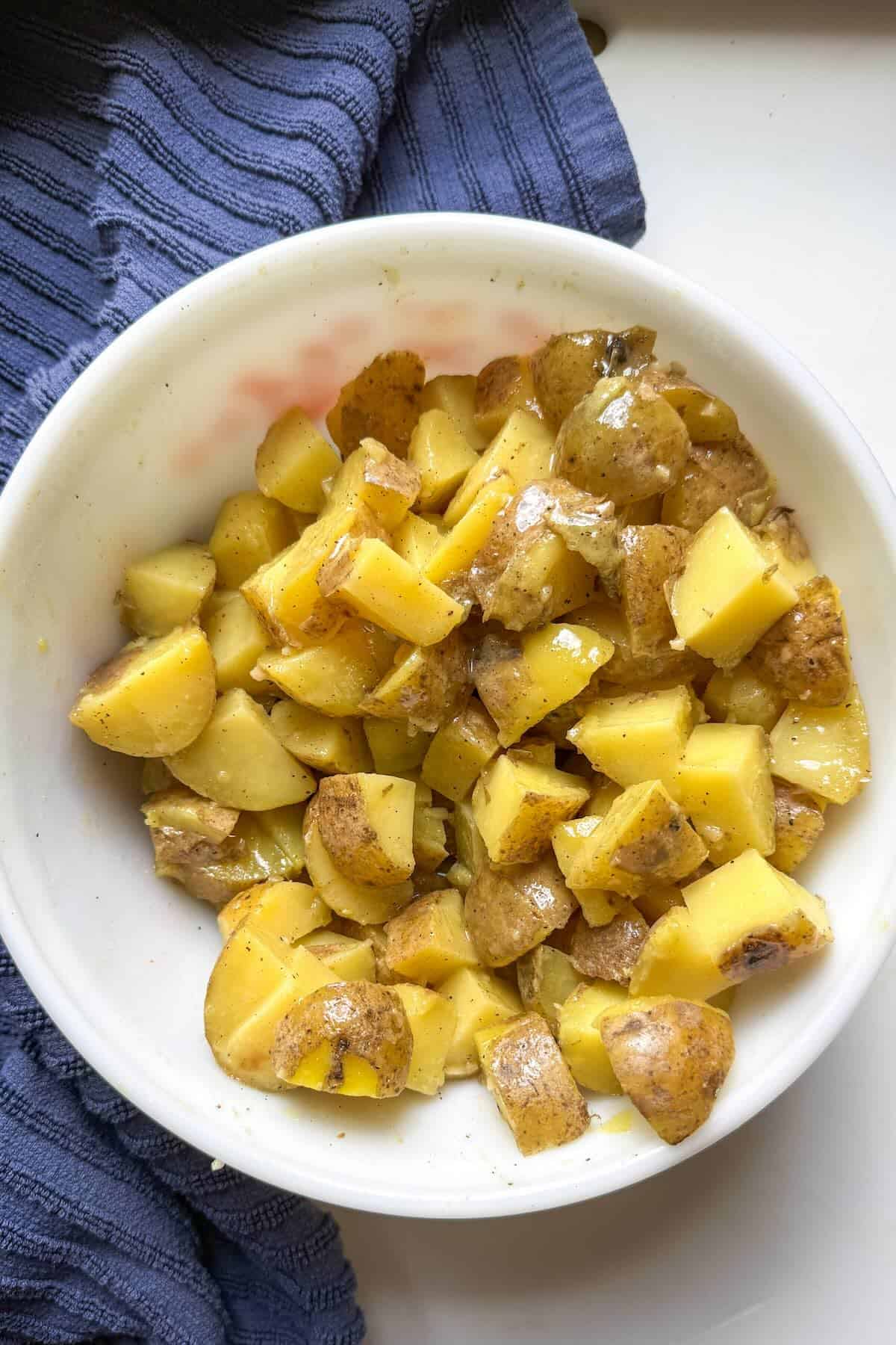 Mixing warm potatoes with dressing to create creamy no mayo potato salad without mayonnaise.