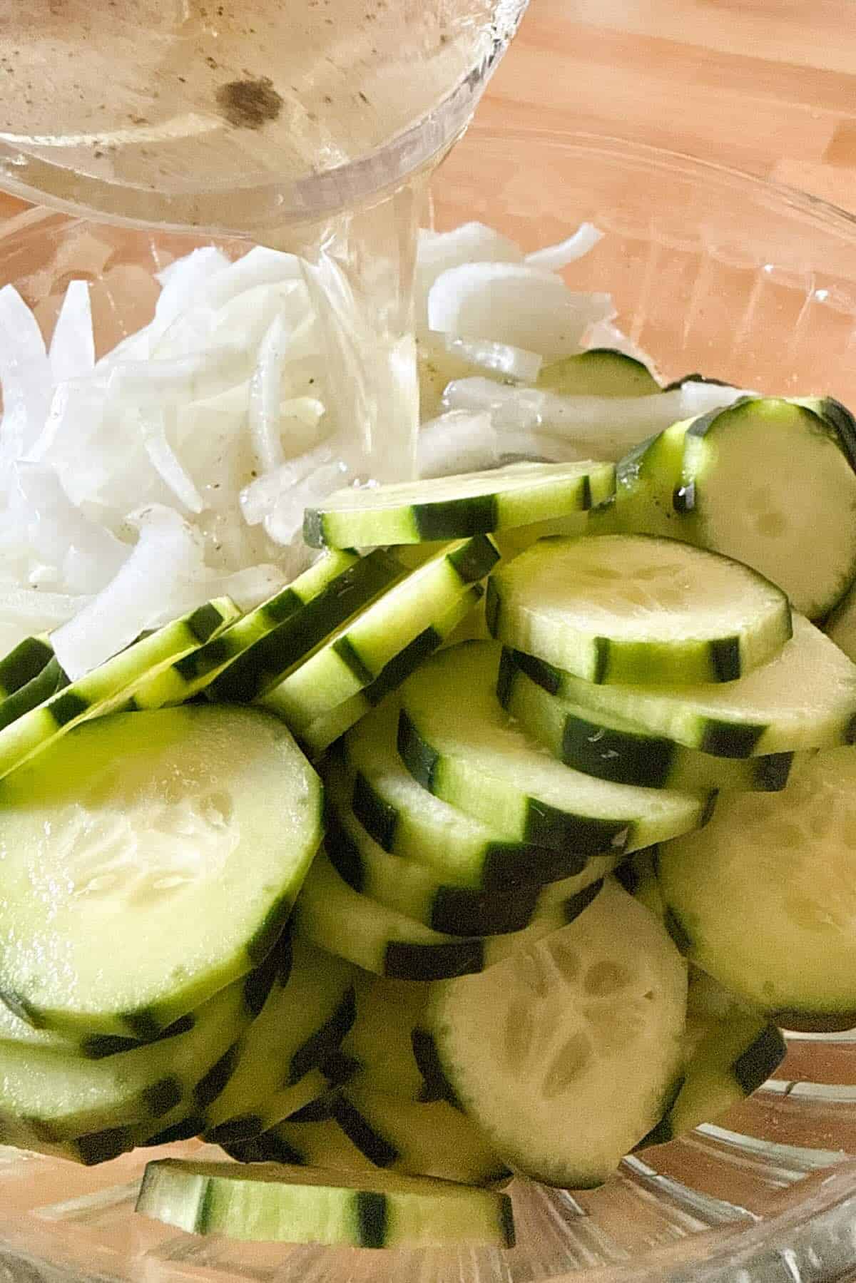 Pouring vinegar marinade over cucumbers and onions.