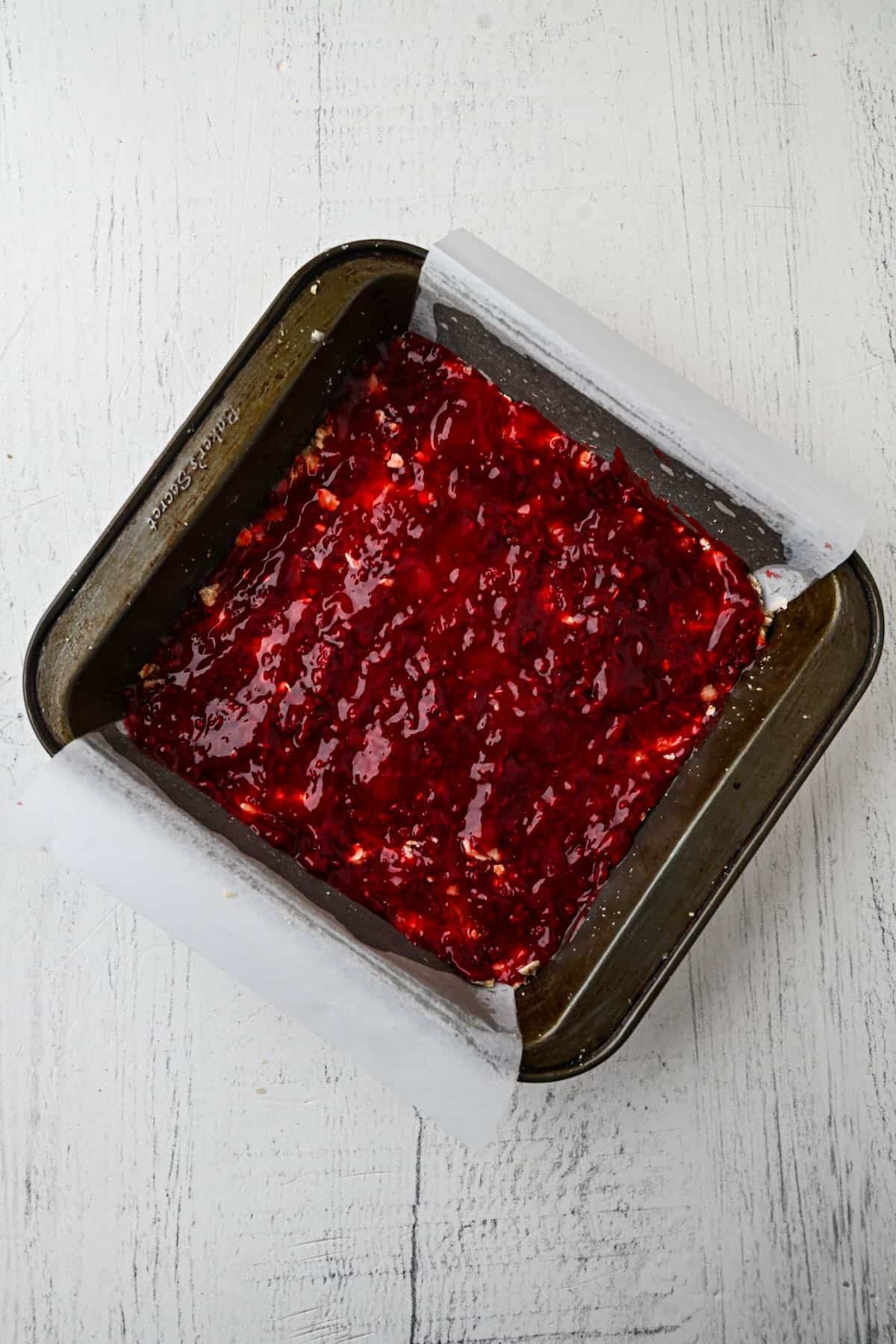 Raspberry jam spread evenly over the oatmeal crust before adding the crumble topping.