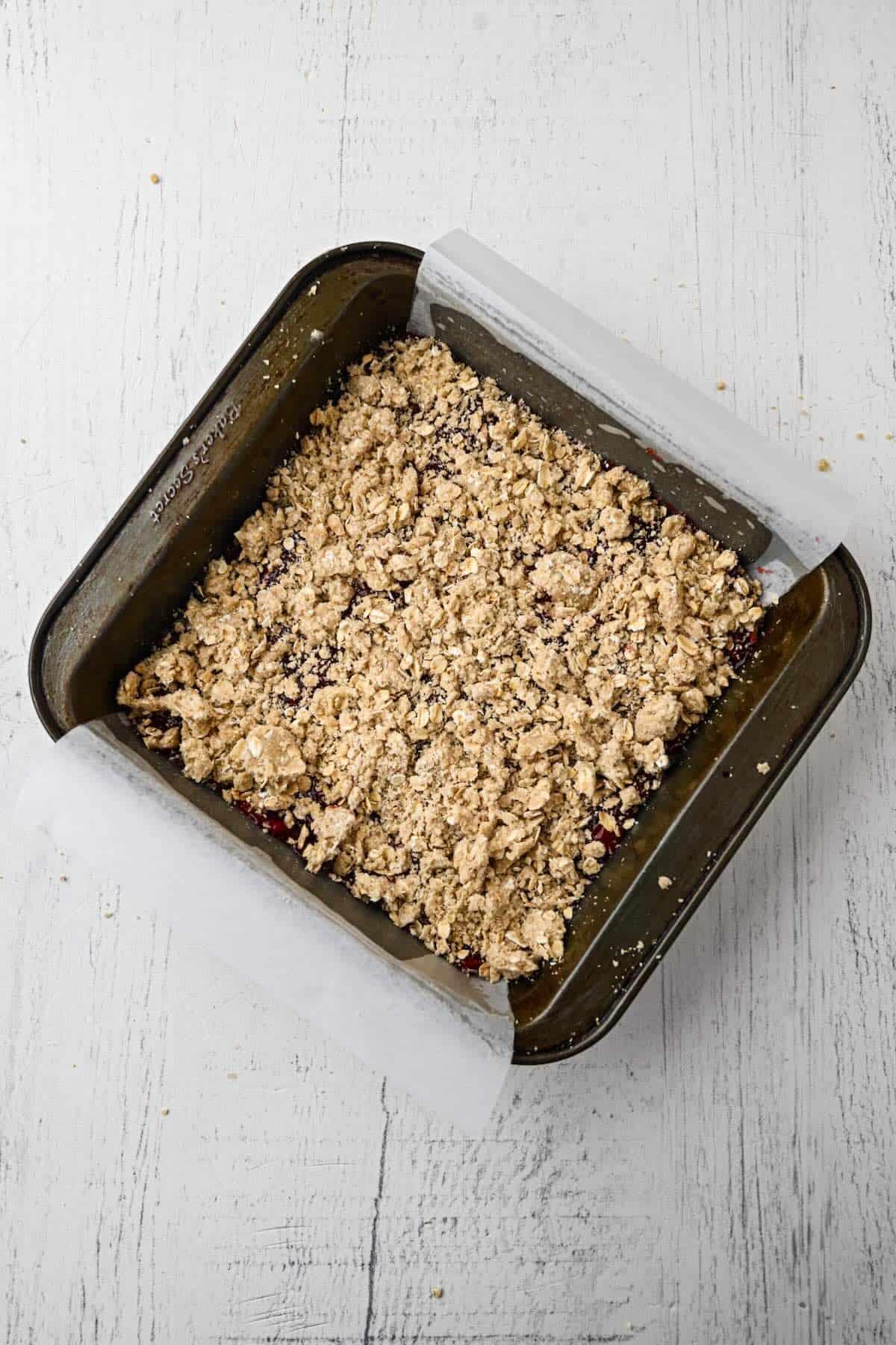 Oat crumble mixture pressed into the bottom of a parchment-lined baking pan to form the crust.