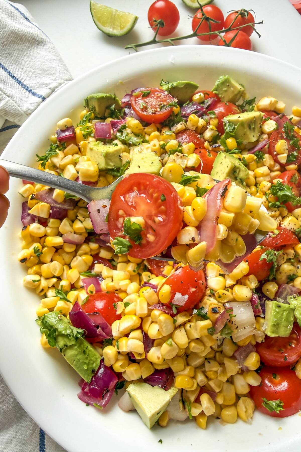Serving spoon scooping grilled corn salad with avocado and charred corn.