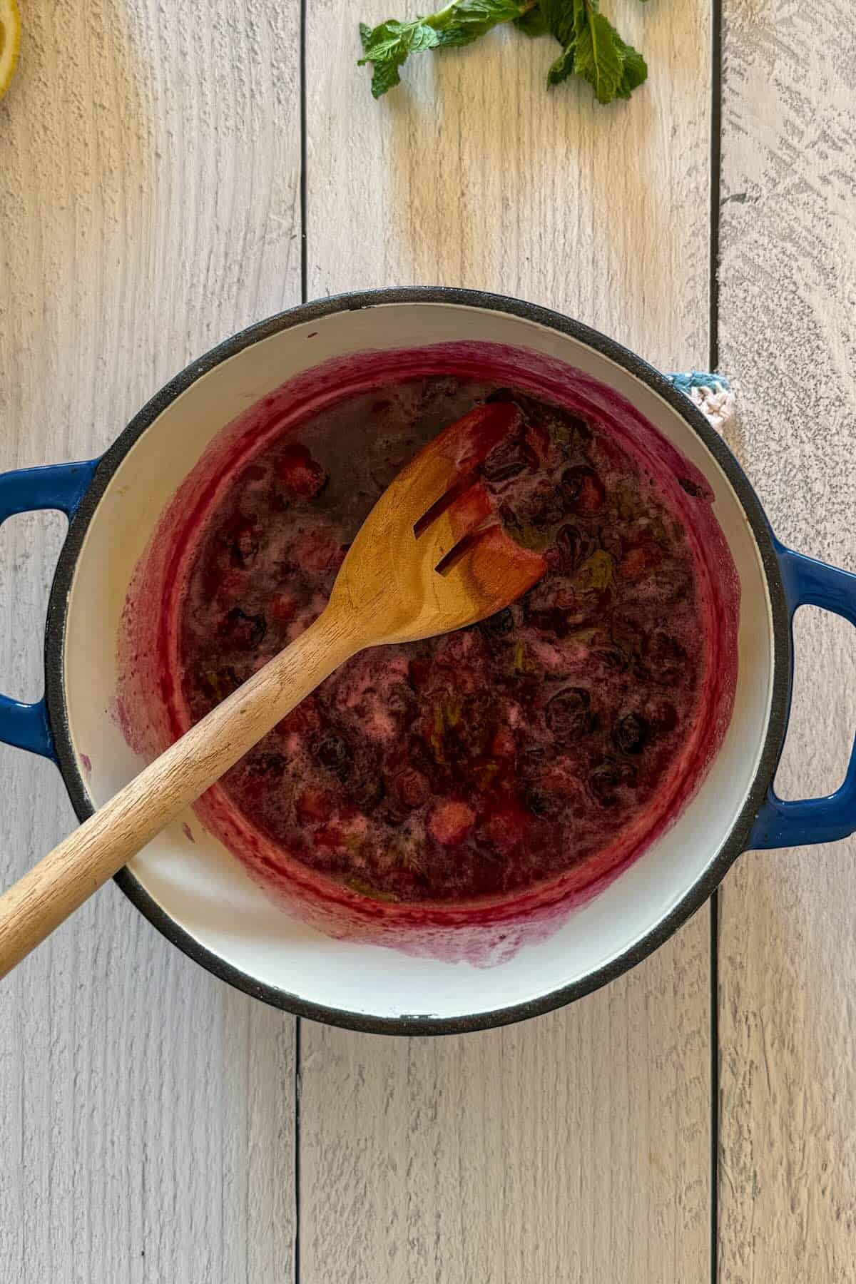 Crushing the blueberries with a wooden spoon to release their juices.