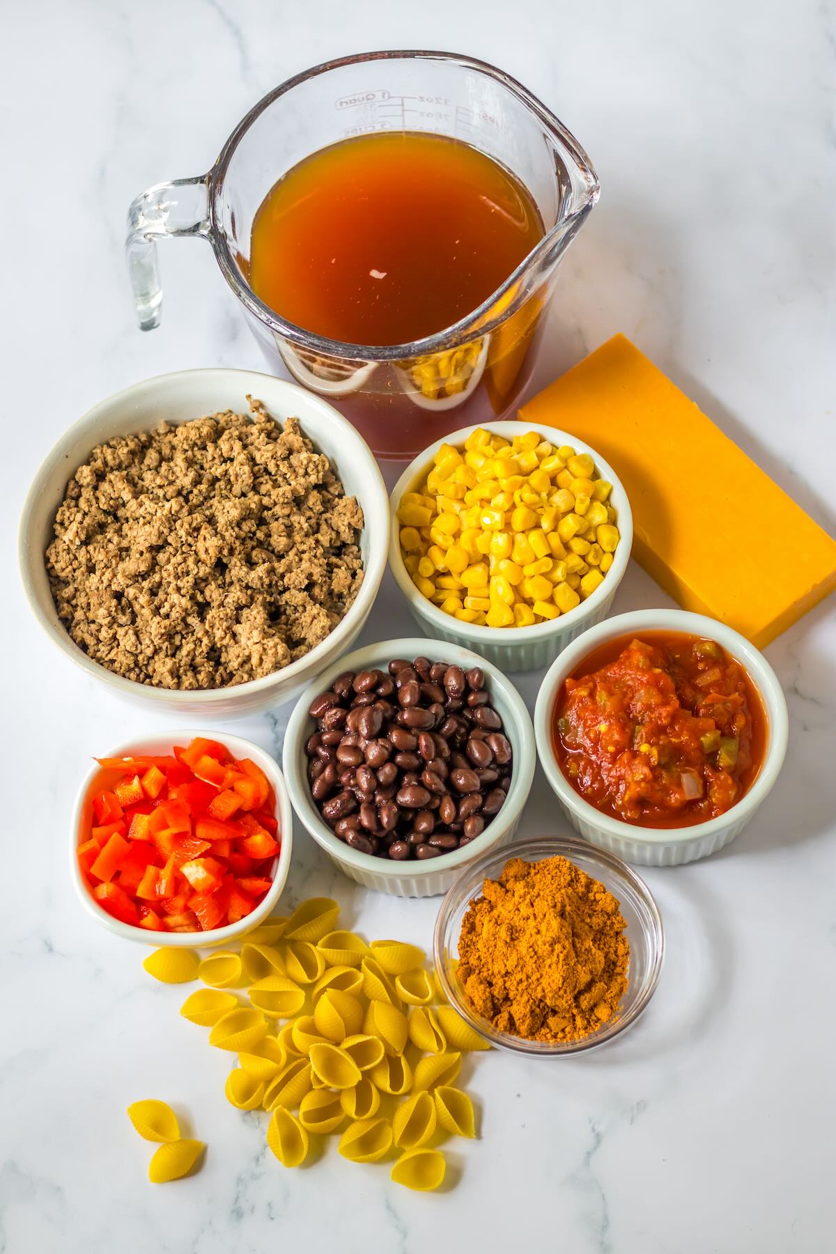 Ingredients for slow cooker taco pasta including ground beef, salsa, black beans, corn, taco seasoning, cheese, and pasta.