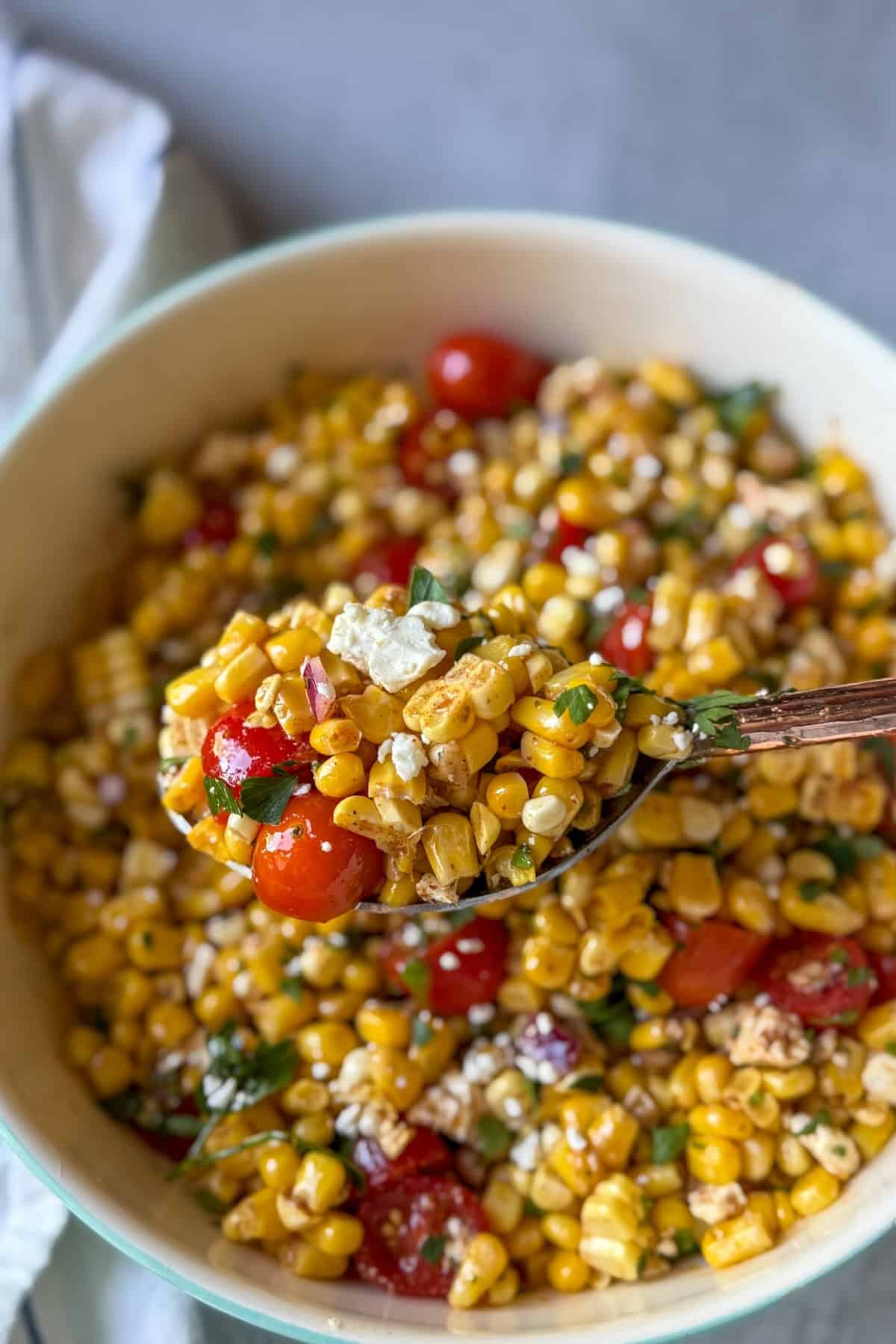 A spoonful of a summer corn salad with juicy tomatoes and crumbled feta cheese.