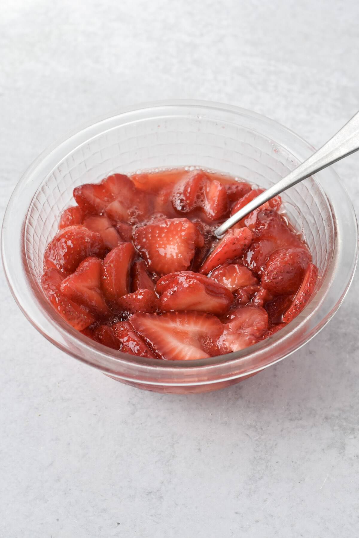 Stirring macerated strawberries in a bowl.