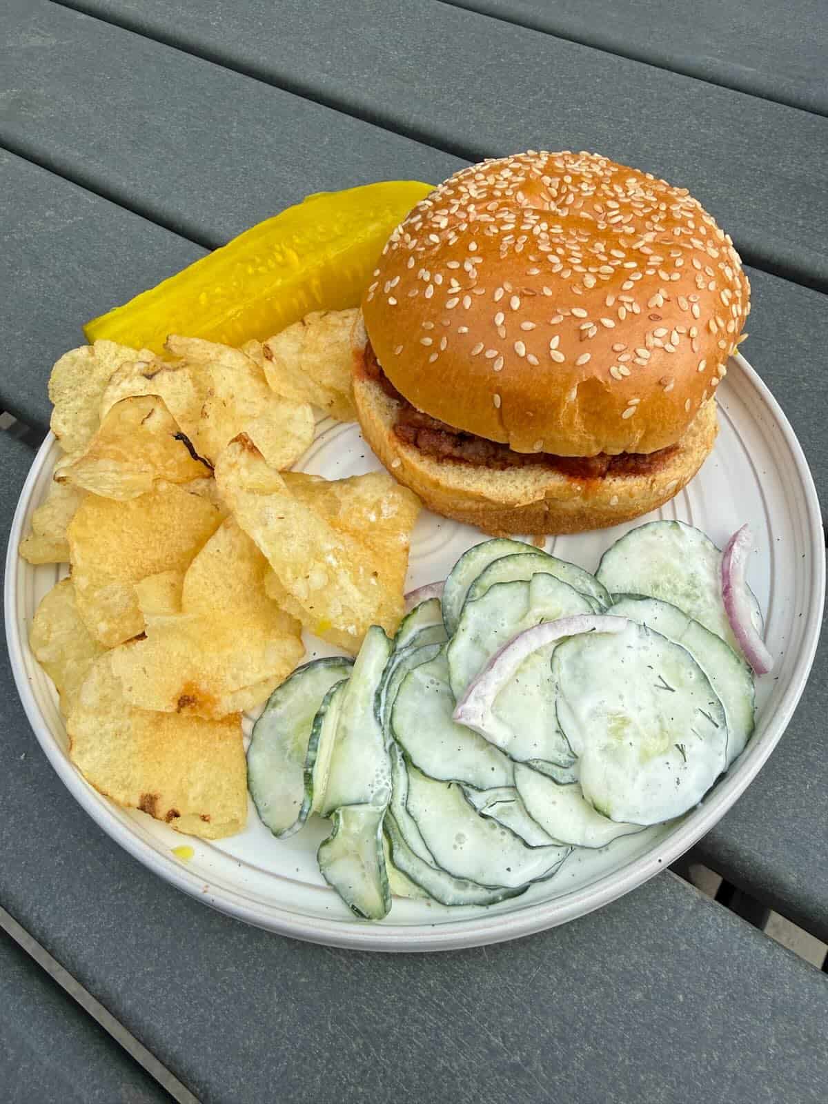 Sloppy joe sandwich with chips and a side of a creamy cucumber salad sprinkled with dill.